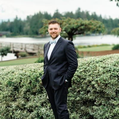 Photo of Louis Jovanovich in front of green shrubs, trees, and a lake.